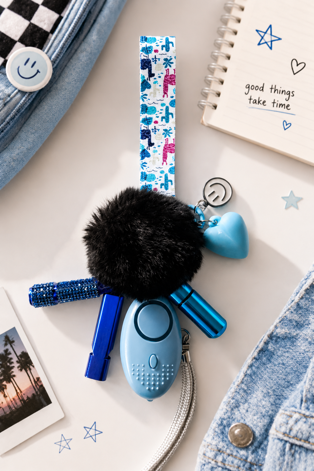 Confidence Club Safety Kit featuring a blue personal safety alarm, LED light, black pom-pom wristlet, blue whistle, and patterned wrist strap