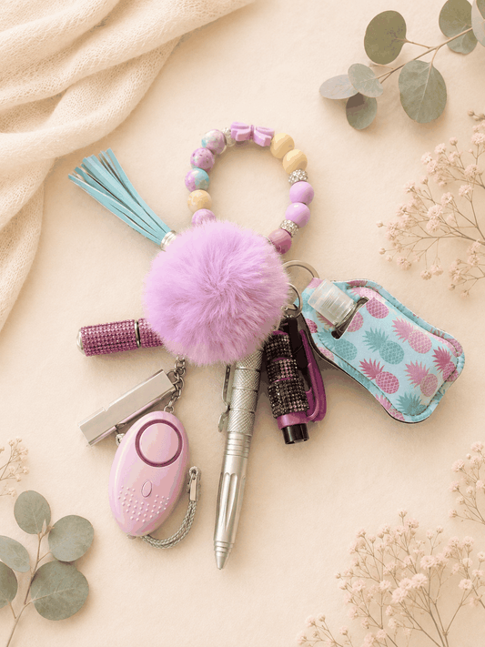 Level-Up Safety Kit keychain with purple pom pom, self-defence pen, personal safety alarm, seatbelt cutter, and pastel beaded wristlet